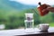 A hand pouring hot water from kettle to make drip coffee with blurred nature background