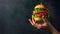 Hand presenting a double cheeseburger on dark backdrop