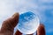 The hand of a psoriasis patient holds a glass ball in which a blue sky with clouds is reflected. A symbol of hope for recovery.
