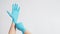 Hand is pulling blue latex gloves on white background