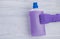 Hand in a purple glove holding a bottle with floor cleaner and floor on grey background