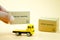 Hand put miniature cardboard boxes on yellow toy truck carries