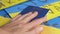 Hand Puts a Biometric Passport of Ukraine on a Background of Ukrainian Flag