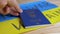 Hand Puts a Biometric Passport of Ukraine on a Background of Ukrainian Flag