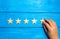 A hand puts the fifth wooden star on a blue background. The critic sets the quality rating. Five stars, the highest quality mark.