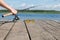 Hand puts a fishing rod with a reel next to sun glasses on a wooden pier
