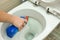 The hand puts a liquid detergent under the rim of the toilet bowl