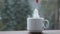 A hand puts a pack of tea into a white cup on a windowsill against a background of snowy weather. Snowfall, winter