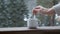 A hand puts a pack of tea into a white cup on a windowsill against a background of snowy weather. Snowfall, winter