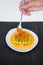 Hand puts red salmon caviar on Mini asparagus with sauce on white plate