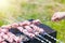 Hand puts skewer with pieces of meat for a shish kebab barbeque on outdoors grill with green blurry background