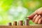 Hand putting coin on coins stack with greenery blurred background