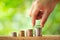 Hand putting coin on coins stack with greenery blurred background