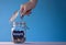 Hand putting a coin in a glass jar with coins with a chalk donate tag on a blue background. Donation and charity concept
