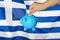 Hand putting coin to piggy bank on Greece flag background