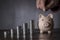 Hand putting coin to piggy bank. Pink piggy bank and money towers on dark background, closeup, copy space. Finance, business,
