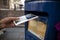 Hand putting a postcard in a Blue Guernsey Post Box unique to Guernsey in the town of St Pierre Port St Peter Port, the main