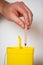 Hand putting used syringe with needle into yellow bin for safe disposal.