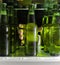 The hand reaches for the beer bottle. Green bottles of beer and drops of condensation are on a shelf in the refrigerator