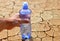 Hand reaches a bottle of water on dry cracked soil.
