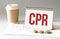 Hand with red pen. Cofee cup. Stick. Keyboard and white background. CPR sign in the notepad