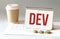 Hand with red pen. Cofee cup. Stick. Keyboard and white background. DEV sign in the notepad