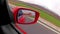 Hand reflection view in a rear view mirror of a fast sport car.