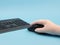 Hand in rubber glove holds a mouse near the keyboard on a blue background.