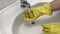 Hand in a rubber yellow glove washes the sink with a sponge.