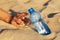 Hand on the sand reaches for a bottle of drinking water. Thirst concept