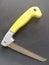 Hand saw for cutting and arranging fruit trees with a yellow handle on a black background,folding saw macro isolated