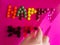 The hand that says happy with colored dragees on a pink background