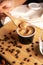 Hand scooping coffee ice cream in a paper cup with wooden spoon on a wooden cutting board with messy coffee beans decoration