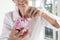 Hand of senior woman putting coins into piggy bank,Smiling elderly holding a piggy bank pink pig feel happy,saving money for