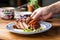 hand serving grilled pork belly on a ceramic plate