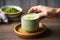 hand serving hot matcha latte on wooden table