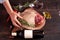 Hand serving a piece of juicy, seasoned rib eye steak wrapped in paper and burlap on a cutting board on a wooden background