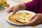 hand serving a piece of peshwari naan on a white plate