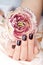 Hand with short manicured nails colored with dark purple nail polish and flower