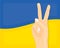 Hand showing victory sign and wavy Ukraine flag