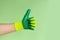 Hand sign thumbs up. Male hand in a glove for working in the garden, vegetable garden on a green background. Copy space