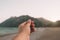 A hand simulates holding a photo, postcard or note on beautiful sunset over the mountains at the beach in summer day.