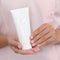 Hand skin care. Female hands holding one white cream tube against body in pink cloth, beautiful beautician woman hands with