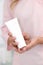 Hand skin care. Female hands holding one white cream tube against body in pink cloth, beautiful beautician woman hands with