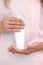 Hand skin care. Female hands holding one white cream tube against body in pink cloth, beautiful beautician woman hands with