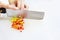 Hand slicing chili pepper vegetable with kitchen knife on chopping board white background