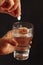 Hand with a soluble pill from headache over the glass of water on black background.