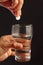 Hand with a soluble pill over the glass of water on black background.