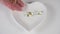 A hand spills a bunch of yellow transparent medical capsules onto a white heart-shaped plate on a white table