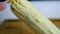 Hand spreading mayonnaise on corn above wooden cutting board